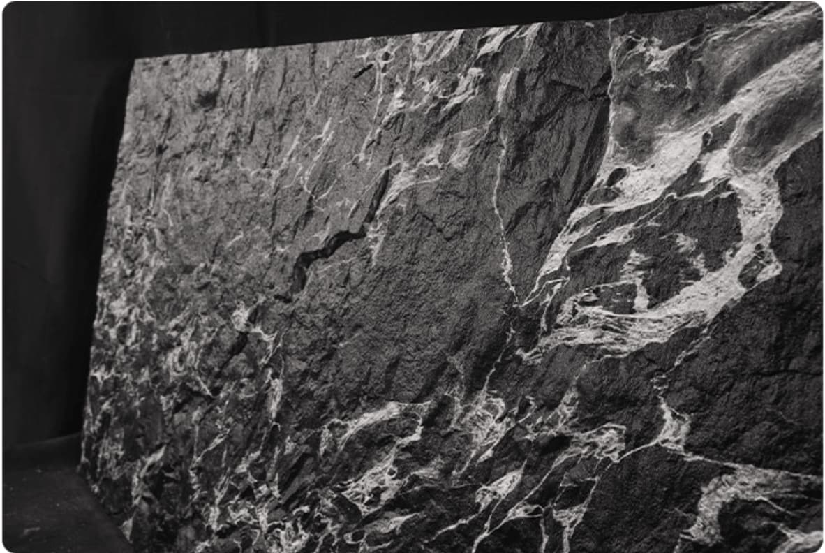 Veined Black Basalt flexible stone veneer – full sheet angled view showing flexibility with dramatic silver-white vein network on deep black textured surface, black background