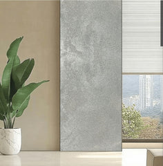 Satin Platinum metallic flexible wall panel installed as full-height interior feature panel beside floor-to-ceiling window – cool silver hammered foil surface with iridescent shimmer in natural daylight, white potted bird-of-paradise plant and city skyline view