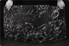  Veined Black Basalt flexible stone panel – full sheet held by gloved hands demonstrating lightweight flexibility, bold silver-white vein network on deep black surface, black background